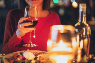 Frau trinkt Rotwein und sitzt bei Essen mit Kerze
