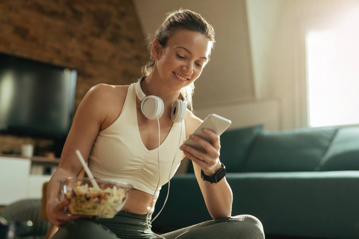 Frau hält Smartphone und isst nach sport