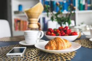 Croissant und Handy liegen mit Kaffee und Erdbeeren auf dem Tisch