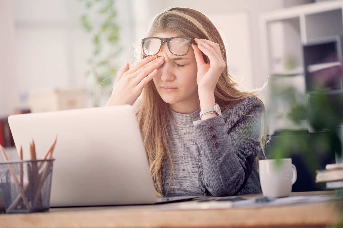 Frau reibt sich Augen unter Brille vor Laptop am Schreibtisch