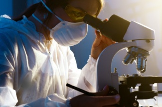 Frau schaut mit Schutzmaske in ein Mikroskop