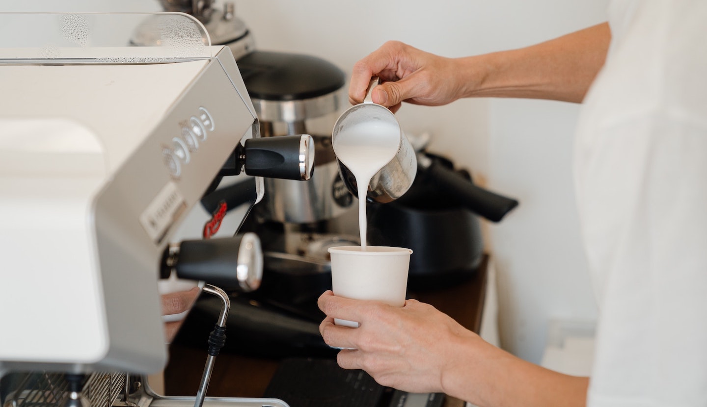 Barista schüttet Milchschaum in Kaffeebecher