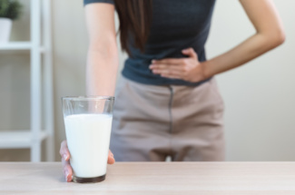 Milchglas vor Frau die verkrampft ihren Bauch hält