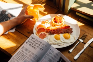 Person sitzt vor Frühstück und liest Zeitschrift