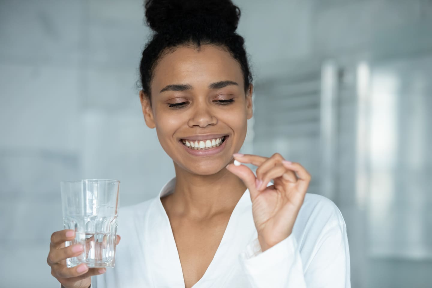 Frau im Badezimmer hält Pille und Wasserglas in Händen