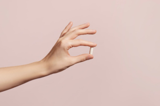 Pille zwischen Zeigefinger und Daumen vor rosa Wand