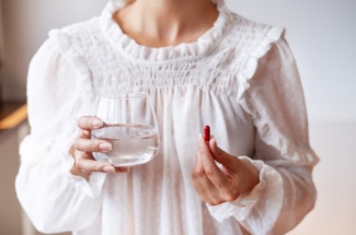 Frau in weissem Kleid hält Wasserglas und rote Pille