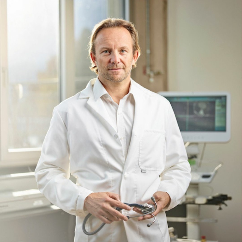 Mann in weißem Kittel hält Stetoskop 