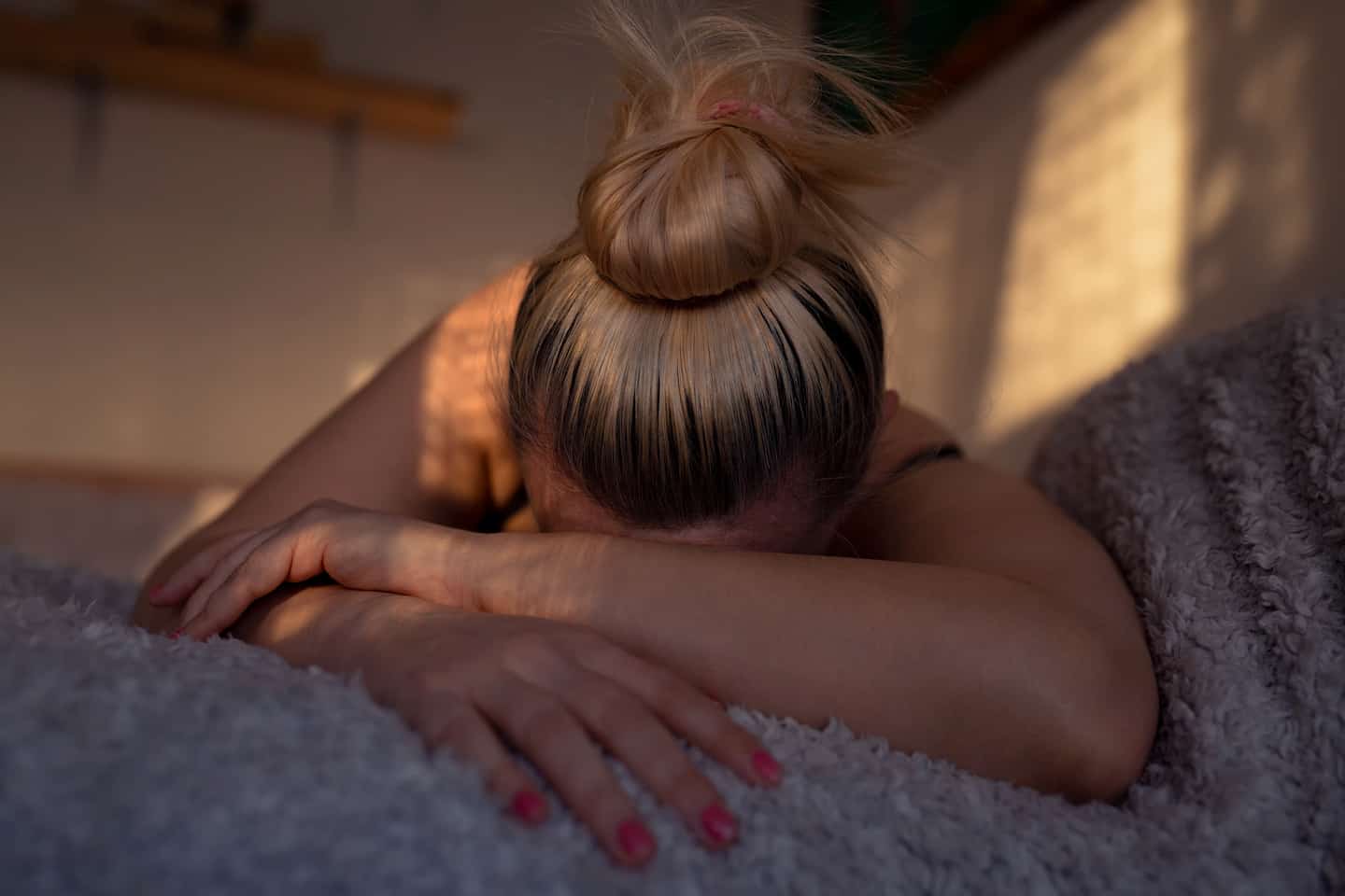 Frau liegt bei gedämmtem Licht mit verschränkten Armen auf dem Bett