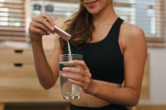 Frau schüttet Pulver aus Sachet in Wasserglas