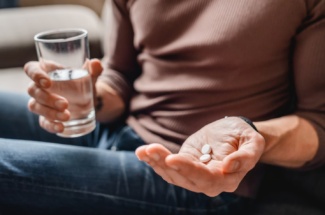 Person hält Wasserglas und Pillen in den Händen
