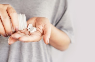 Person schüttet Tabletten aus weißer Kunststoffdose in die Hand