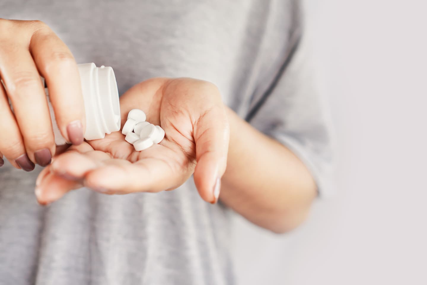 Person schüttet Tabletten aus weißer Kunststoffdose in die Hand