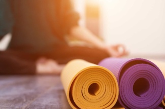 Person meditiert im Hintergrund hinter zwei aufgerollten Yogamatten
